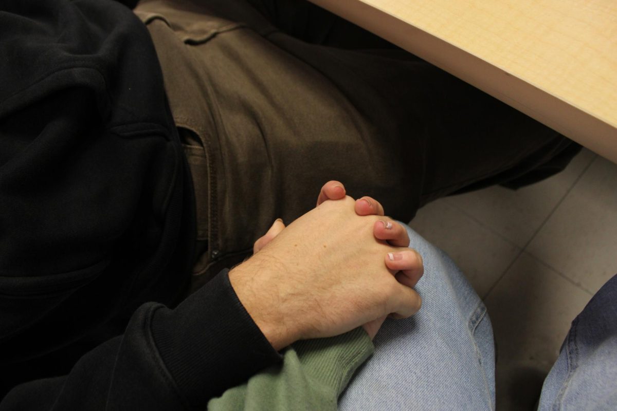 Two seniors hold holds under the table in class. 